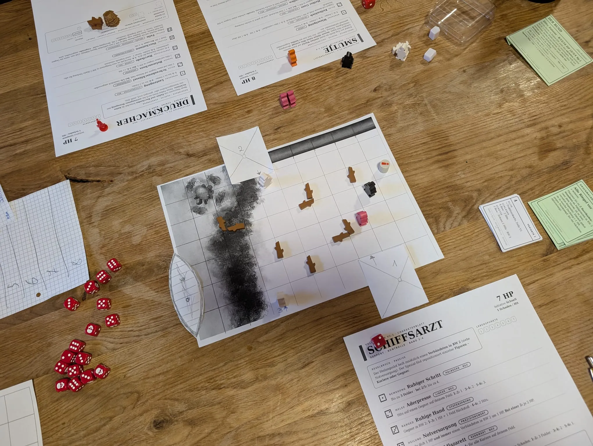 Ausgedrucktes Papierspielfeld auf einem Holztisch, darauf Holzfiguren, daneben rote Würfel und mehrere Charakterbögen